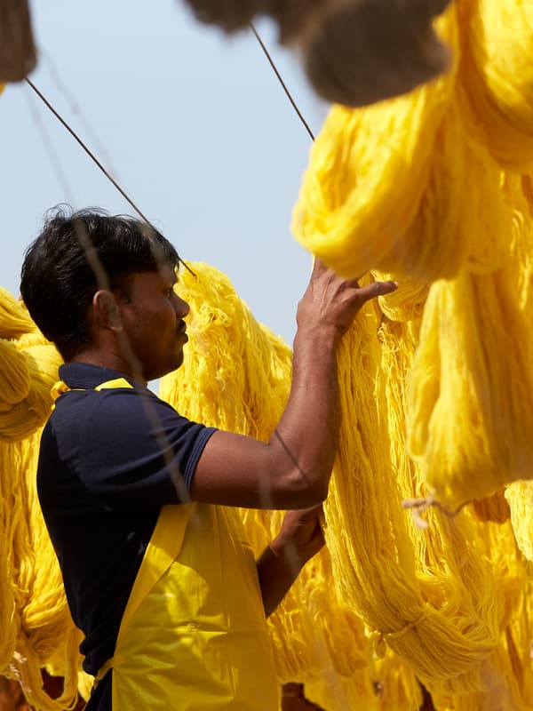 Un homme vêtu d’un t-shirt noir et d’un tablier jaune étend du coton jaune vif, récemment teint, à l’extérieur pour le faire sécher.