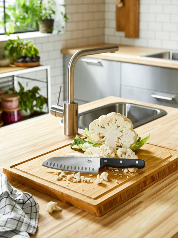 Un îlot de cuisine avec un plan de travail en bois, un bloc style billot APTITLIG arborant un couteau de cuisine, et un chou-fleur coupé.