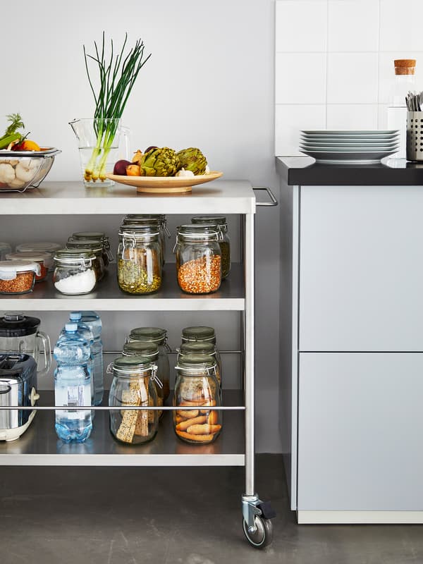 Un îlot de cuisine en métal près d’un comptoir de cuisine, avec plusieurs bocaux en verre contenant des aliments secs et des légumes.