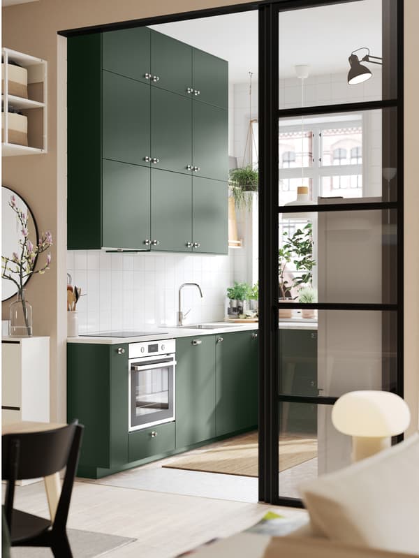 Un ingresso ampio su una cucina con frontali HAVSTORP verde scuro e piano di lavoro EKBACKEN bianco effetto marmo/laminato.