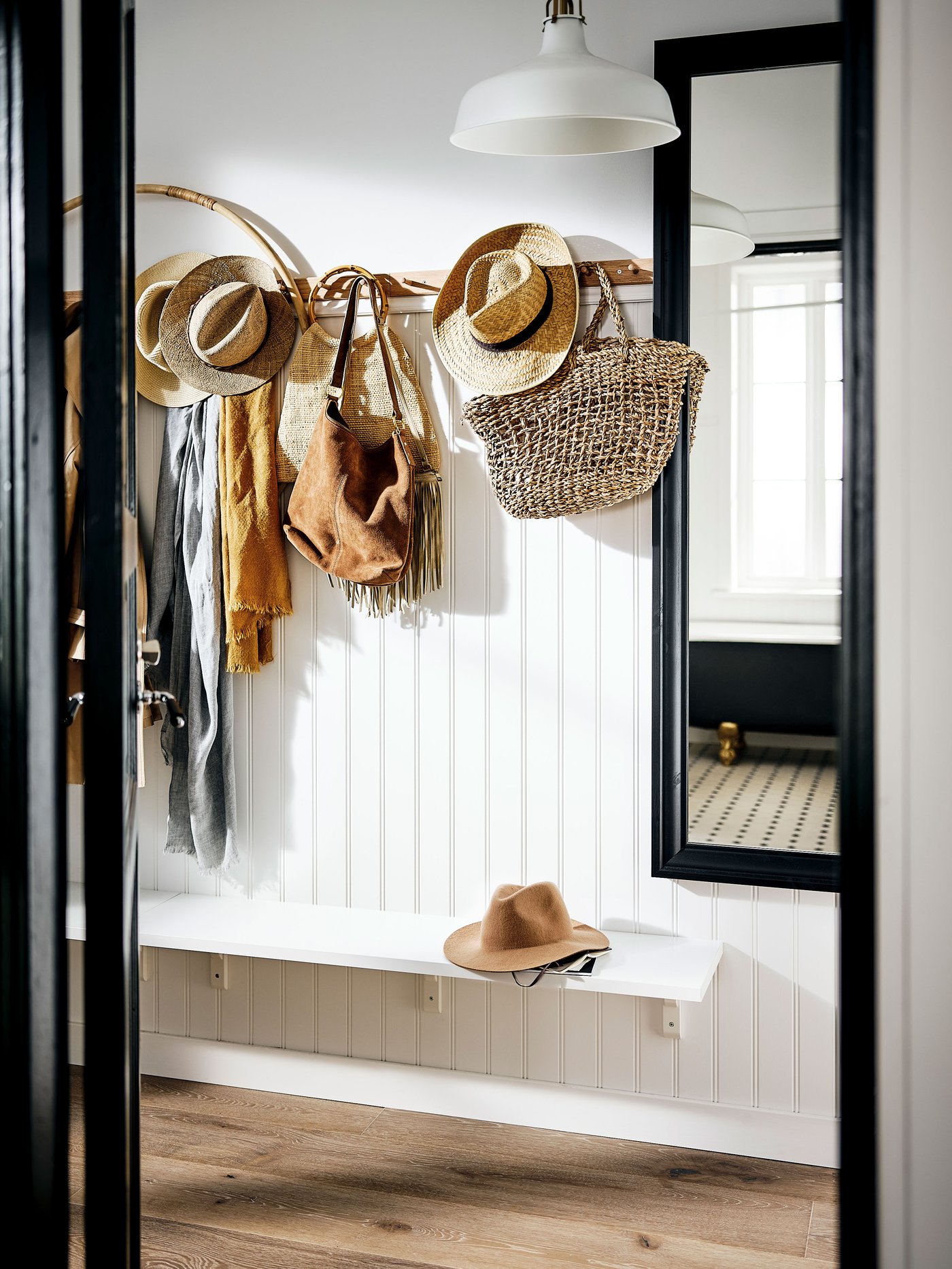 Un ingresso con uno specchio con cornice nera e una mensola bianca con sopra un cappello. C'è un attaccapanni a cui sono appesi diversi accessori.