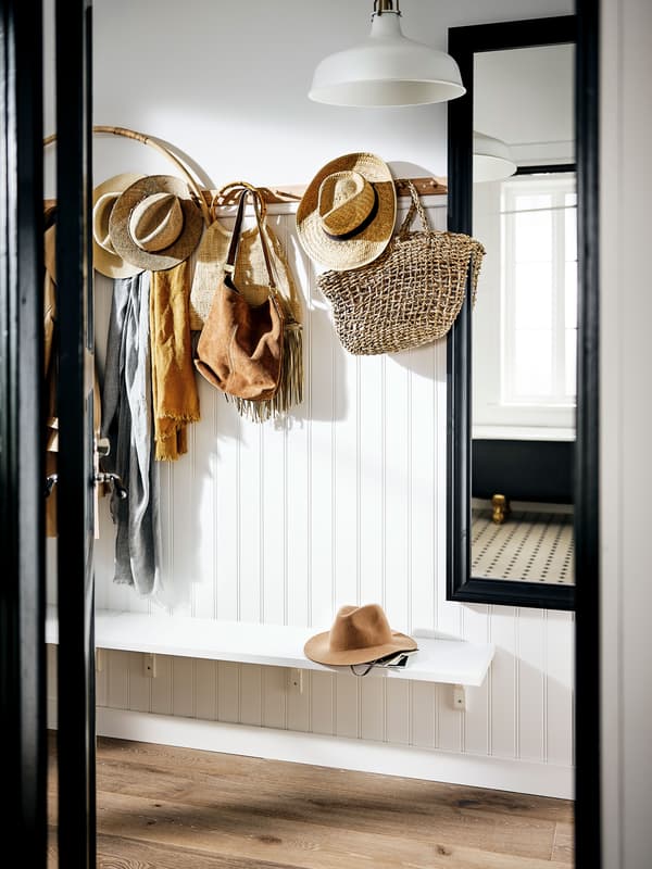 Un ingresso con uno specchio con cornice nera e una mensola bianca con sopra un cappello. C'è un attaccapanni a cui sono appesi diversi accessori.