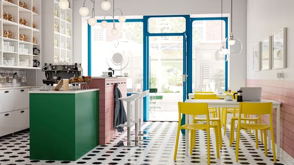 Un intérieur de café-bar clair et aéré, avec un sol en carrelage noir et blanc, une palette de couleurs vives et de grandes fenêtres donnant sur la rue.