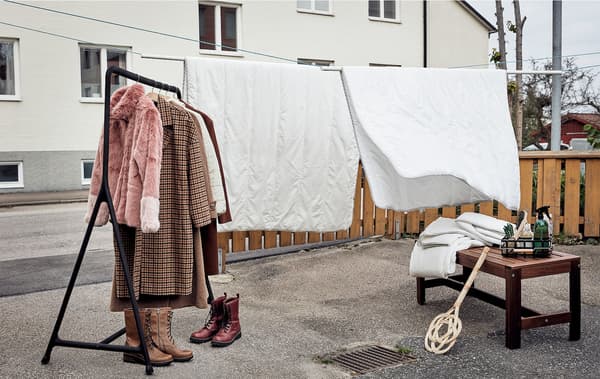 Un jardin avant asphalté, prêt pour le ménage du printemps : des couettes suspendues à une corde à linge, un portant, des souliers, des vêtements et des accessoires de nettoyage.