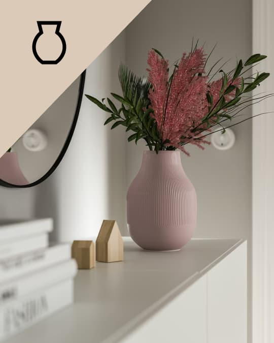 Un jarron rosa sobre un mueble con una planta con flor roja.