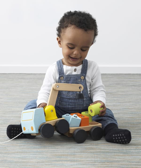 Un jeune enfant joue avec une grue en bois et des cubes.