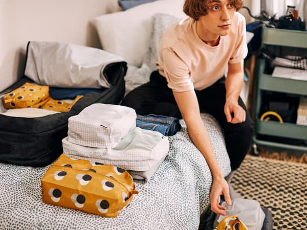 Un jeune étudiant est assis sur son lit entouré de choses qu’il prévoit d’emporter au collège, soigneusement rangées dans des sacs RENSARE.