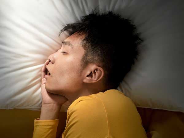 Un jeune homme couché sur le côté dort profondément sur l'oreiller ergonomique IKEA PRAKTVÄDD.