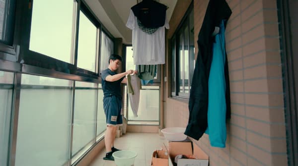 Un jeune homme fait sécher des vêtements dans un balcon fermé en briques et en verre.