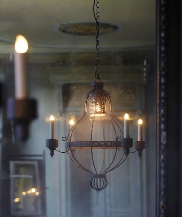 Un lampadario con 4 candelieri appeso in una stanza dai toni crema e una porta ornata sullo sfondo.