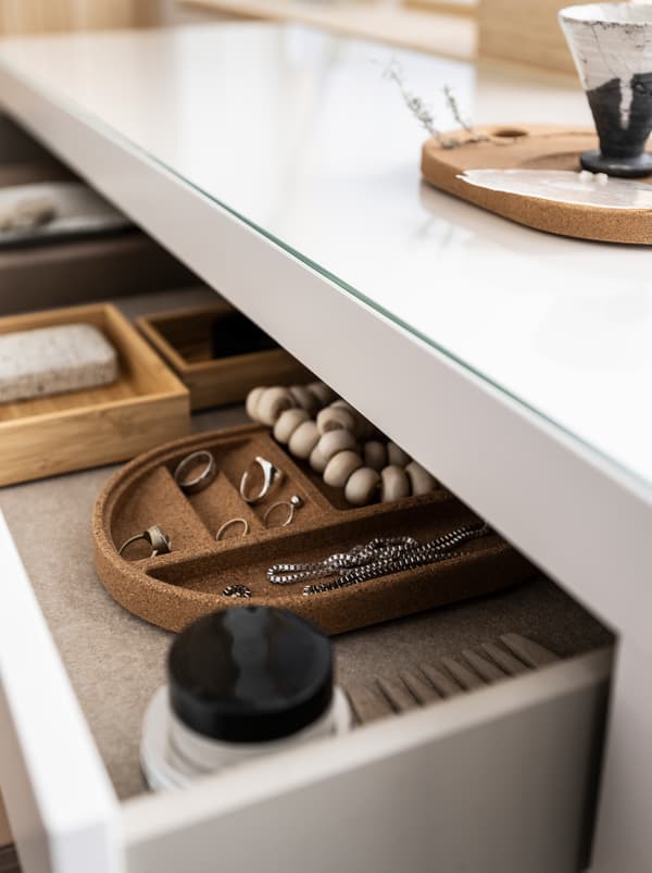 Un large tiroir de commode ouvert, peu profond, laissant apparaître des bijoux et des accessoires de beauté, certains dans des plateaux SAXBORGA.