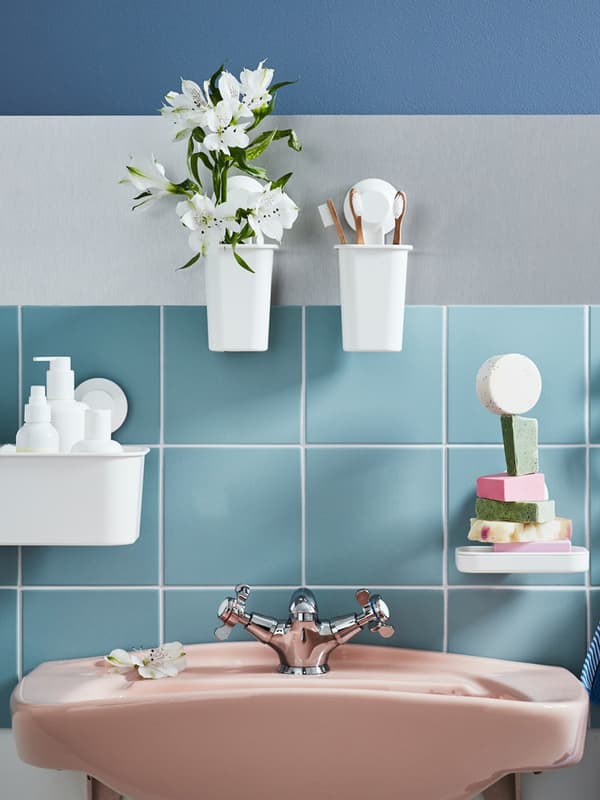 Un lavabo rosa con alcuni supporti a muro contenenti diversi oggetti tra cui portasaponi, saponi, spazzolini, fiori.