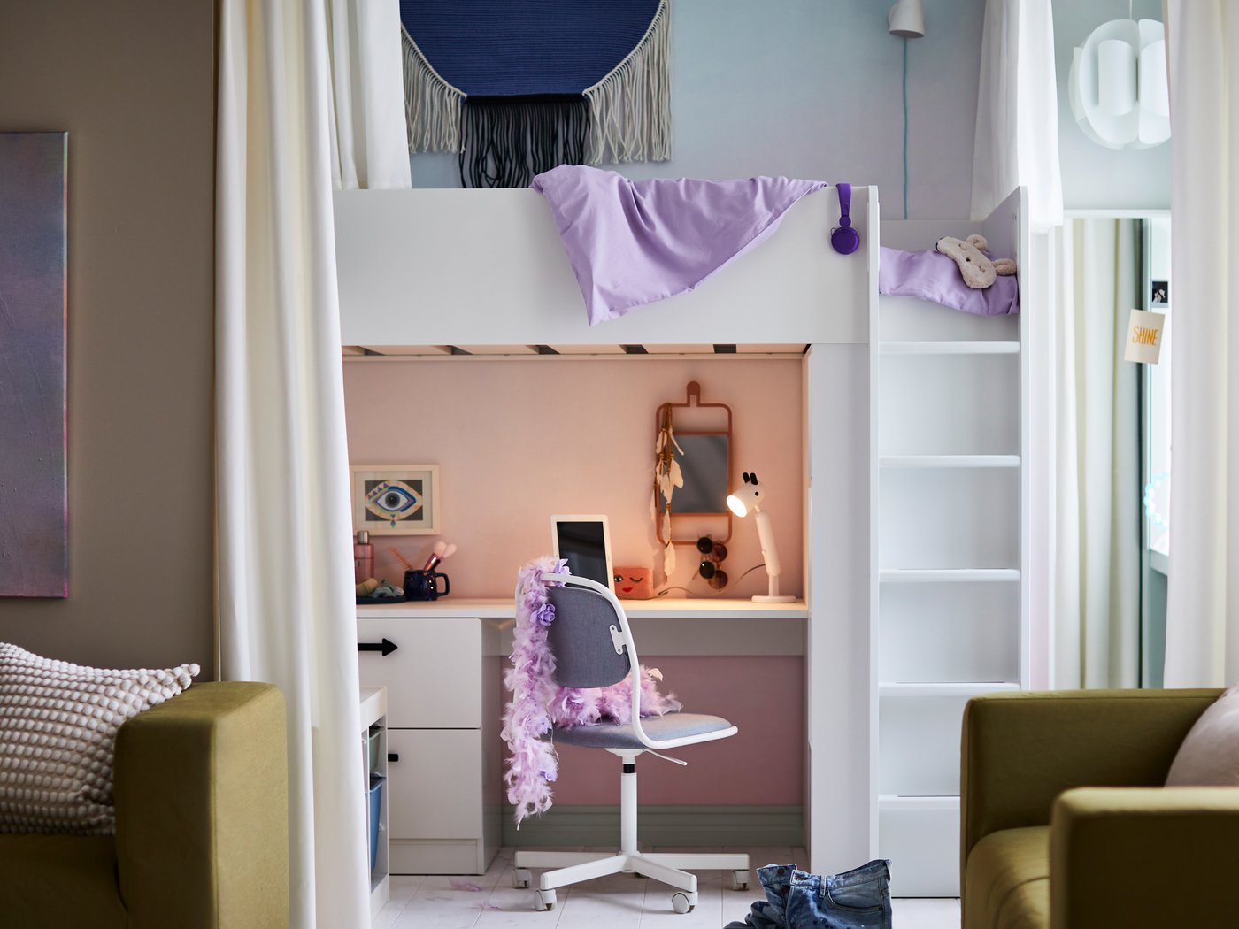 Un letto a soppalco SMÅSTAD bianco con scrivania accanto a una sedia girevole ÖRFJÄLL con un boa di piume viola drappeggiato sullo schienale - IKEA.