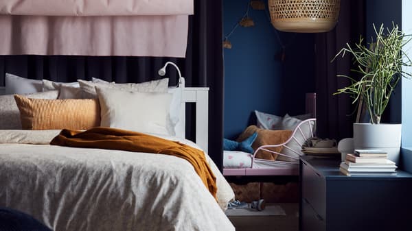Un letto allungabile accanto a un letto bianco con biancheria da letto beige/bianco, un cuscino beige scuro, tende rosa e una lampada a sospensione in bambù - IKEA