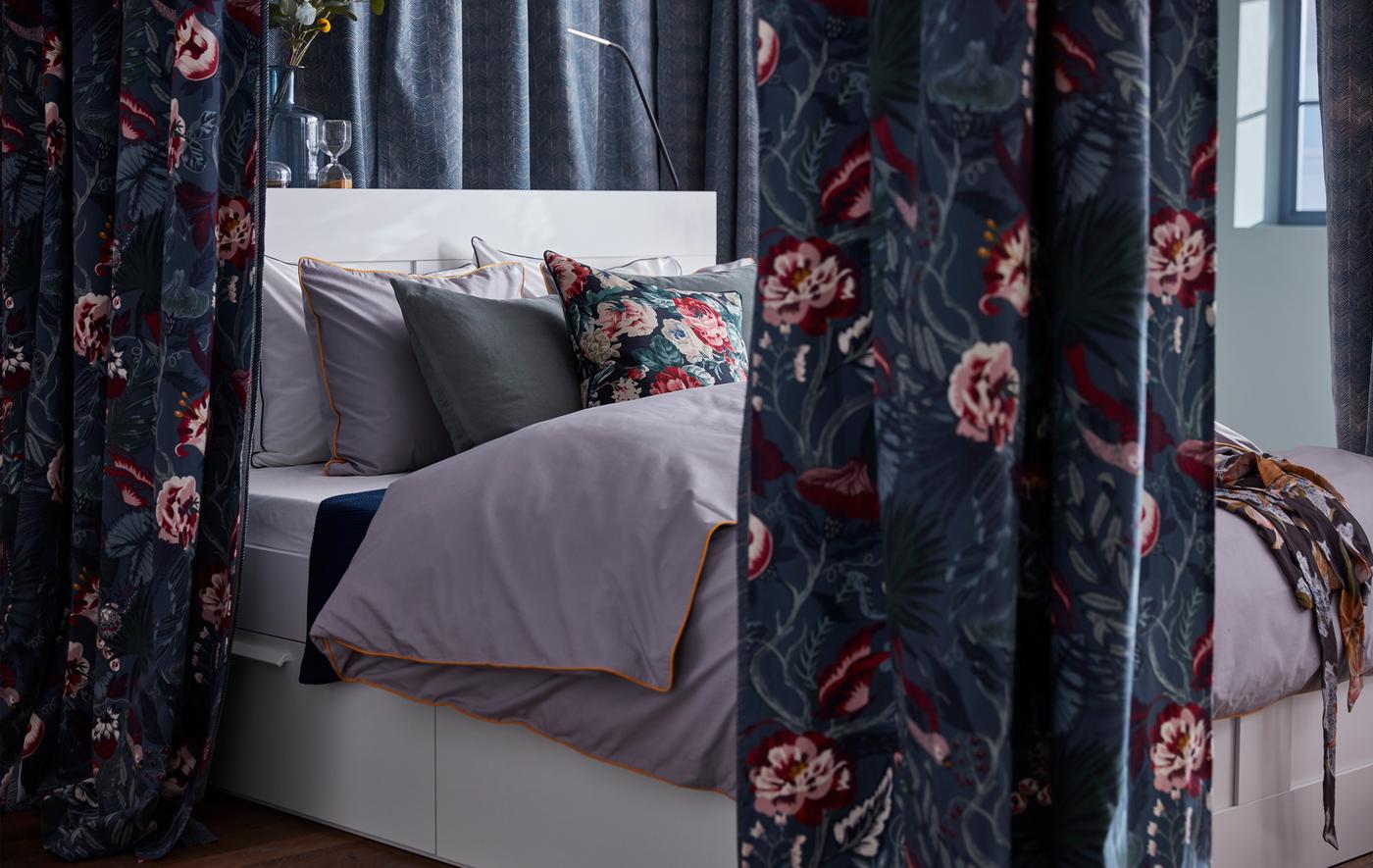 Un letto circondato da tende realizzate con il tessuto a metraggio FILODENDRON dal motivo floreale in blu scuro - IKEA