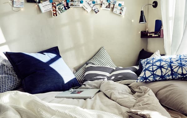 Un letto con biancheria dai colori neutri e cuscini a motivo grafico bianco e blu - IKEA