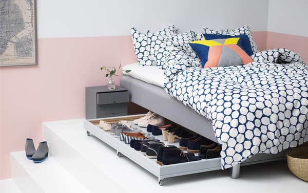 Un letto con contenitore aperto al cui interno si trovano delle scarpe.