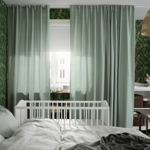 Un letto e un lettino accanto a una finestra con tende verdi/bianche e una tenda a rullo oscurante bianca - IKEA