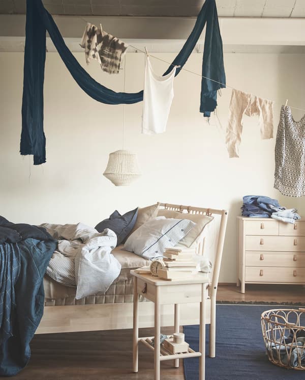 Un letto e un mobile della collezione di mobili per camera da letto BJÖRKSNÄS. Accanto, un comodino con libri e una sveglia. Sopra il letto, un filo con stesi degli indumenti.