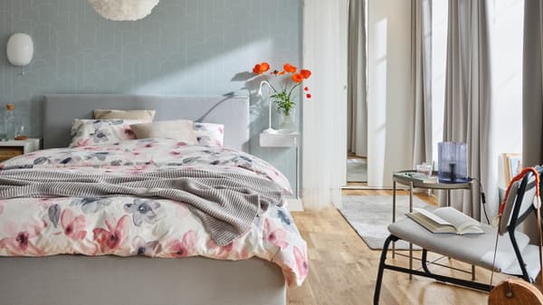 Un letto GLADSTAD in una camera grigia con biancheria da letto LAPPNYCKLAR dal motivo floreale. Accanto, una poltrona e un tavolino - IKEA