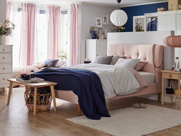 Un letto imbottito IDANÄS con biancheria BERGPALM nel mezzo di una stanza luminosa con un tavolino ai suoi piedi - IKEA.