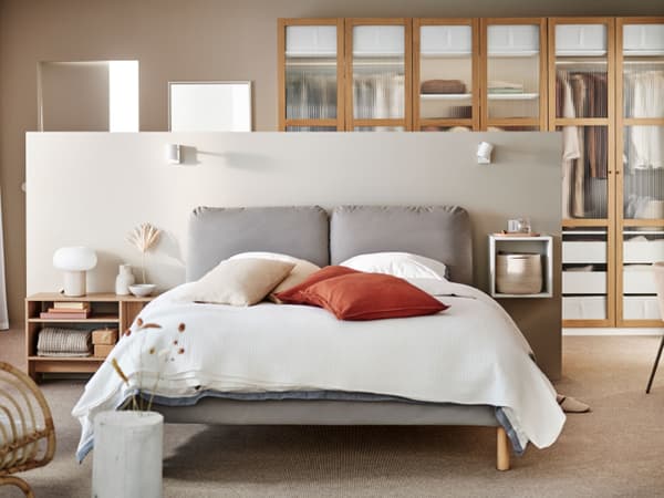 Un letto imbottito SAGESUND in marrone Diseröd/Luröy in un'ampia camera da letto ariosa, rivestito di lenzuola bianche con cuscini rossi.