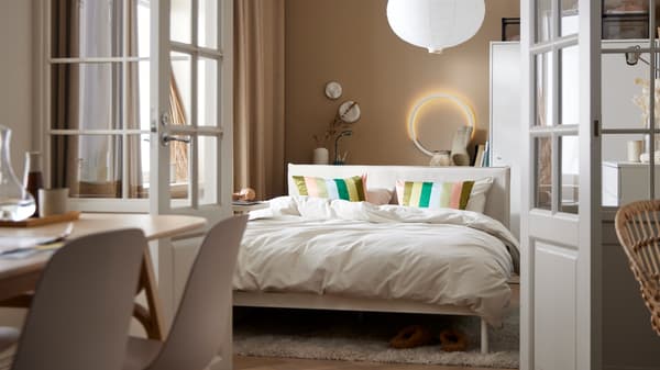 Un letto KLEPPSTAD con biancheria ÄNGSLILJA grigio-beige in una piccola camera sotto a una lampada a sospensione RISBYN - IKEA.