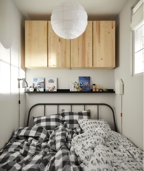 Un lit avec deux duvets, surmonté d’une étagère pour photos accueillant des livres et d’armoires en bois.