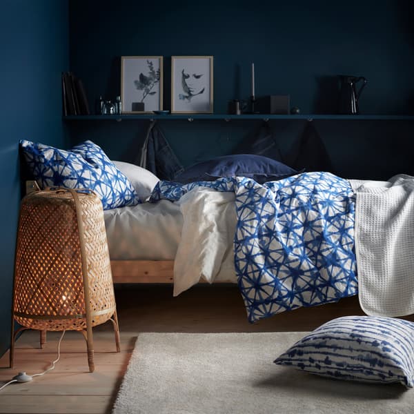 Un lit avec du linge de lit à motif bleu et blanc et un lampadaire dans une chambre aux murs bleu foncé.