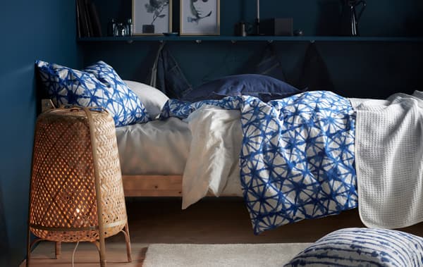 Un lit avec du linge de lit à motif bleu et blanc et un lampadaire dans une chambre aux murs bleu foncé.