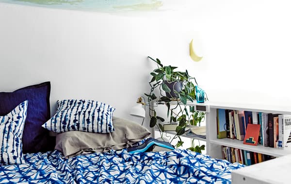 Un lit avec du linge de lit aux motifs bleus et une bibliothèque sur le côté.