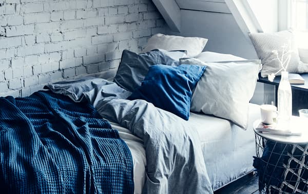 Un lit avec du linge de lit rayé bleu et blanc et des coussins contre un mur de briques peint en blanc.