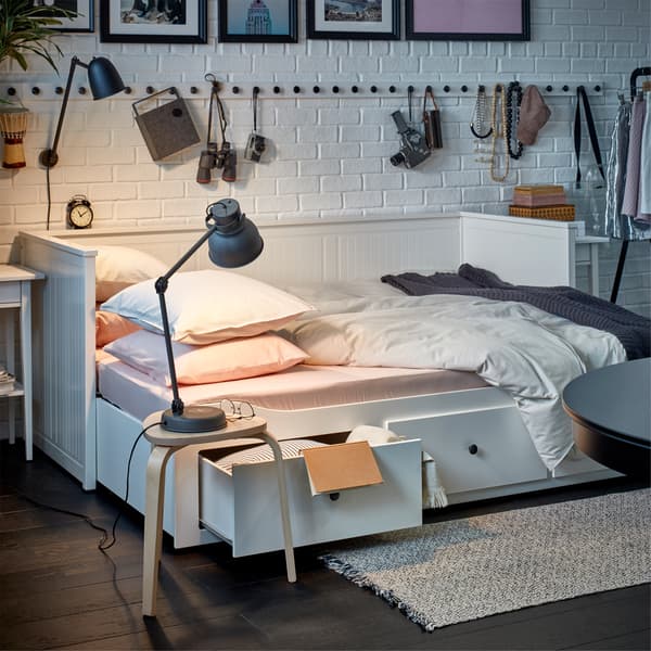 Un lit banquette blanc transformé en lit avec du linge de lit confortable, à côté duquel est posé un tabouret avec une lampe de table allumée.