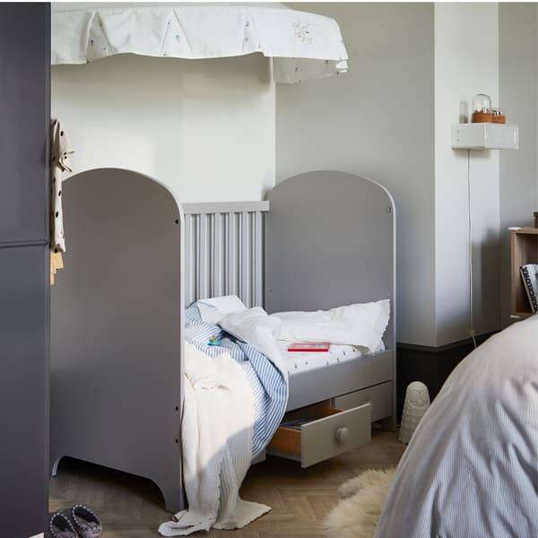 Un lit bébé avec du linge de lit rayé bleu et blanc. Un ciel de lit est fixé au mur au-dessus du lit.