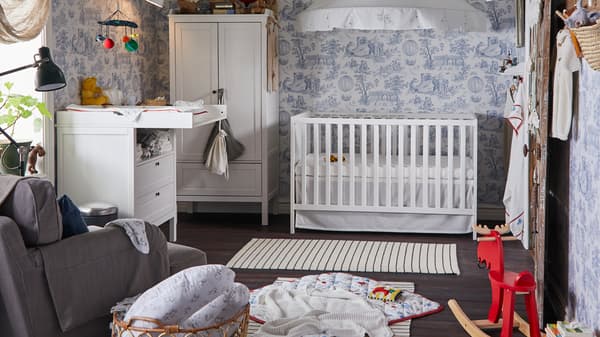 Un lit bébé, une armoire et une table à langer SUNDVIK occupent une chambre d’enfant traditionnelle au papier peint à motifs.