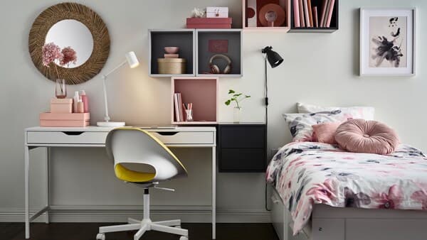Un lit d’appoint blanc BRIMNES avec un linge de lit à motif floral LAPPNYCKLAR, à côté d’un bureau ALEX avec des étagères au-dessus.