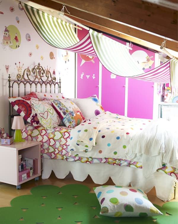 Un lit d’enfant confortable avec une tête de lit en métal et un mélange de motifs colorés sur les oreillers et la housse de couette.