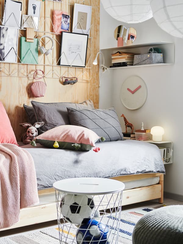 Un lit empilable UTÅKER avec une tonne de coussins, de l’art sur papier au-dessus, une étagère BOTKYRKA comme table de chevet, des rangements et des objets décoratifs.