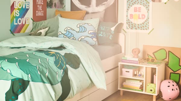 Un lit est habillé d’une housse de couette BLÅVINGAD aux nuances turquoise ; les murs autour sont recouverts d’affiches.