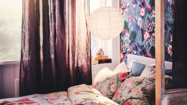 Un lit garni d’un plaid et d’un ensemble housse de couette et taies d’oreiller NÄSSELKLOCKA, sous un abat-jour pour suspension.