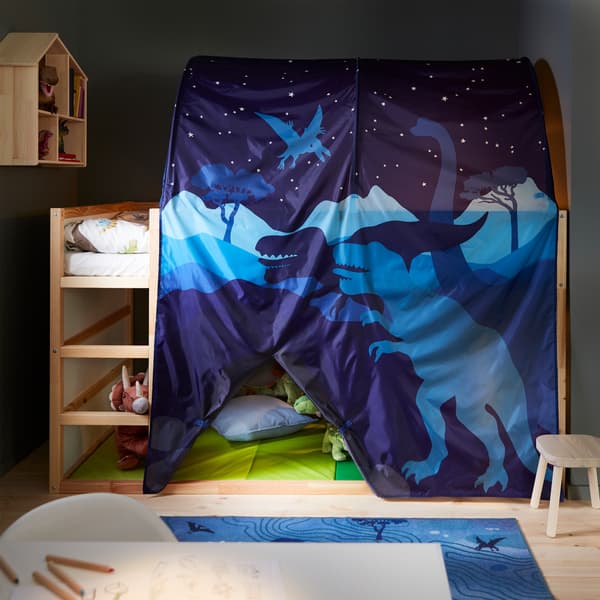 Un lit haut en blanc/pin, un ciel de lit bleu orné d’un motif de dinosaure, un tapis de gymnastique pliant vert, un tapis bleu et un bureau blanc.
