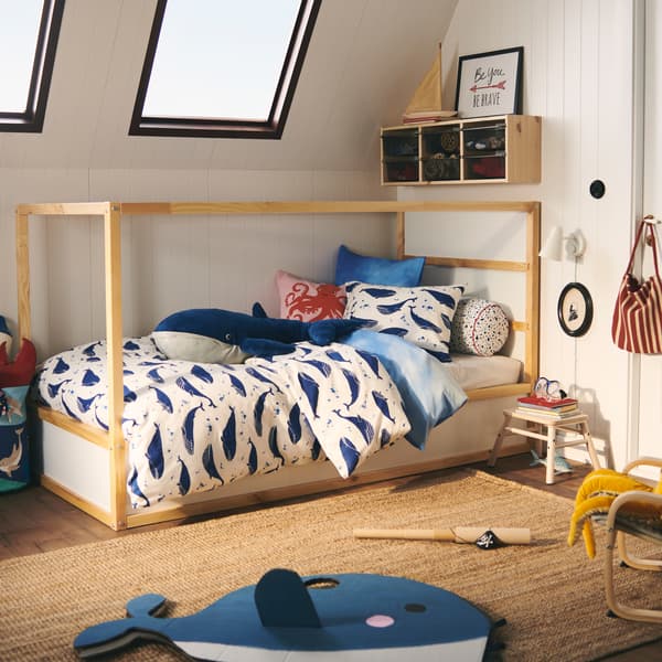 Un lit KURA est habillé d’un ensemble de housse de couette BLÅVINGAD à motif de baleines ; une peluche de baleine bleue BLÅVINGAD se trouve dessus.
