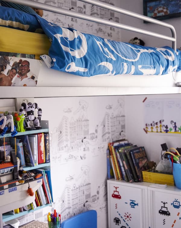 Un lit mezzanine blanc dans la chambre d’un enfant, avec des livres, des étagères et des rangements en dessous.