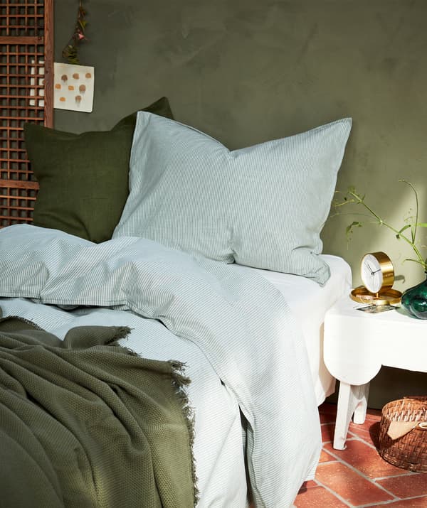 Un lit moelleux avec du linge de lit blanc et vert, deux grands oreillers et des rayons de soleil pénétrant sur la droite.