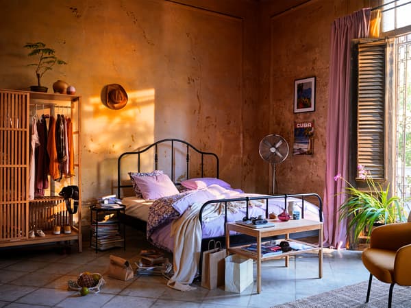 Un lit noir avec un cadre en acier et des détails couleur laiton. Le lit est placé contre un mur orange sur un sol carrelé.