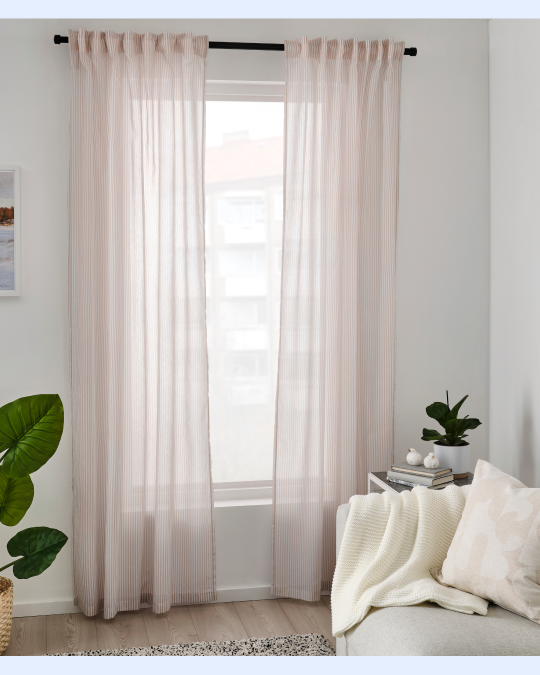 Un living con plantas y un sofá blanco con una manta. En la esquina destacan unas cortinas que filtran la luz.