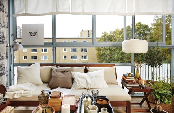 Un living con un sofá cafe claro y cojines que combinan con colores como cafe, blanco y beige. Lampara al lado para iluminar con pantalla redonda y blanca. Una mesa con decoración como canastos, floreros y recipientes.