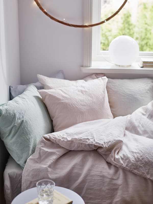 Un llit còmode a la cantonada d'una habitació, coberta de roba de llit tenyida a mà de colors pastel.