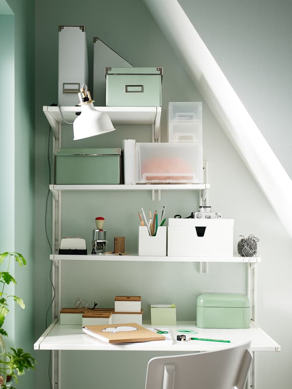 Un lugar de traballo ordenado baixo un teito inclinado que se realizou utilizando estantes de almacenaxe de parede de IKEA de anchos diferentes.