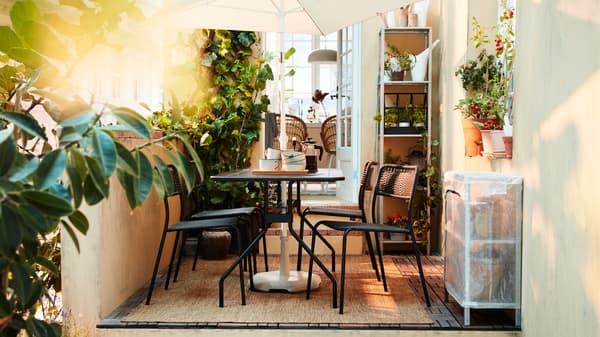 Un lussureggiante spazio all’aperto con un set coordinato di tavolo e sedie in nero, un ombrellone bianco, tante piante e un tappeto - IKEA